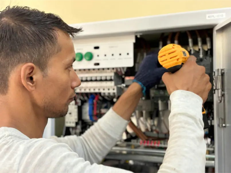 A person uses a yellow power drill to work on an open electrical control panel, showcasing the expertise often provided by top electrical companies.