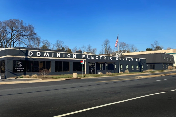 Nuestra historia 8 A single-story building with "Dominion Electric Supply Co." written across the facade, this Electrical Distribution Company is situated beside a road with clear skies and some leafless trees in the background.
