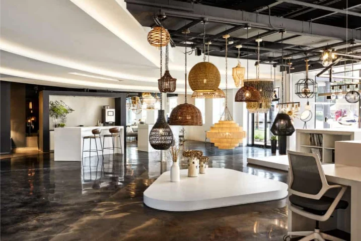 Nuestra historia 9 Modern showroom by an Electrical Distribution Company featuring various hanging light fixtures, a glossy dark floor, white display tables, bar stools, and a desk chair in a spacious, well-lit interior.
