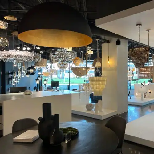A modern showroom by an Electrical Distribution Company displays various contemporary light fixtures and chandeliers, with tables and decor placed throughout the bright, open space.